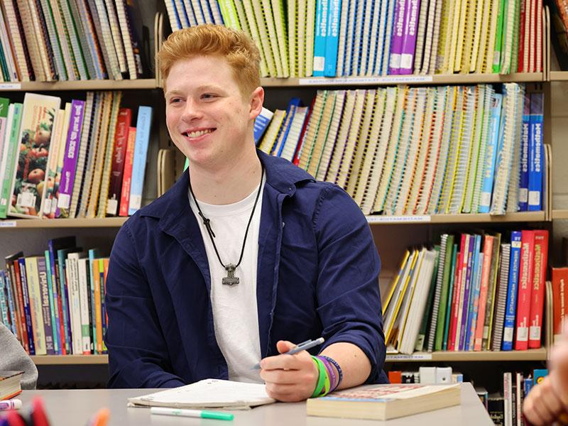 College student working at table, in front of bookshelves